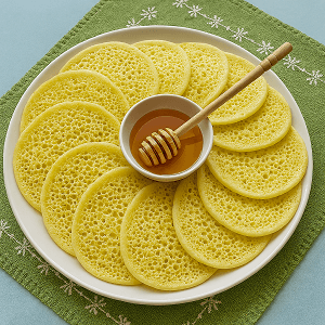 honeycomb pancake delight arranged in a circular pattern on a white plate with a bowl of honey at the center, set on a green embroidered napkin.